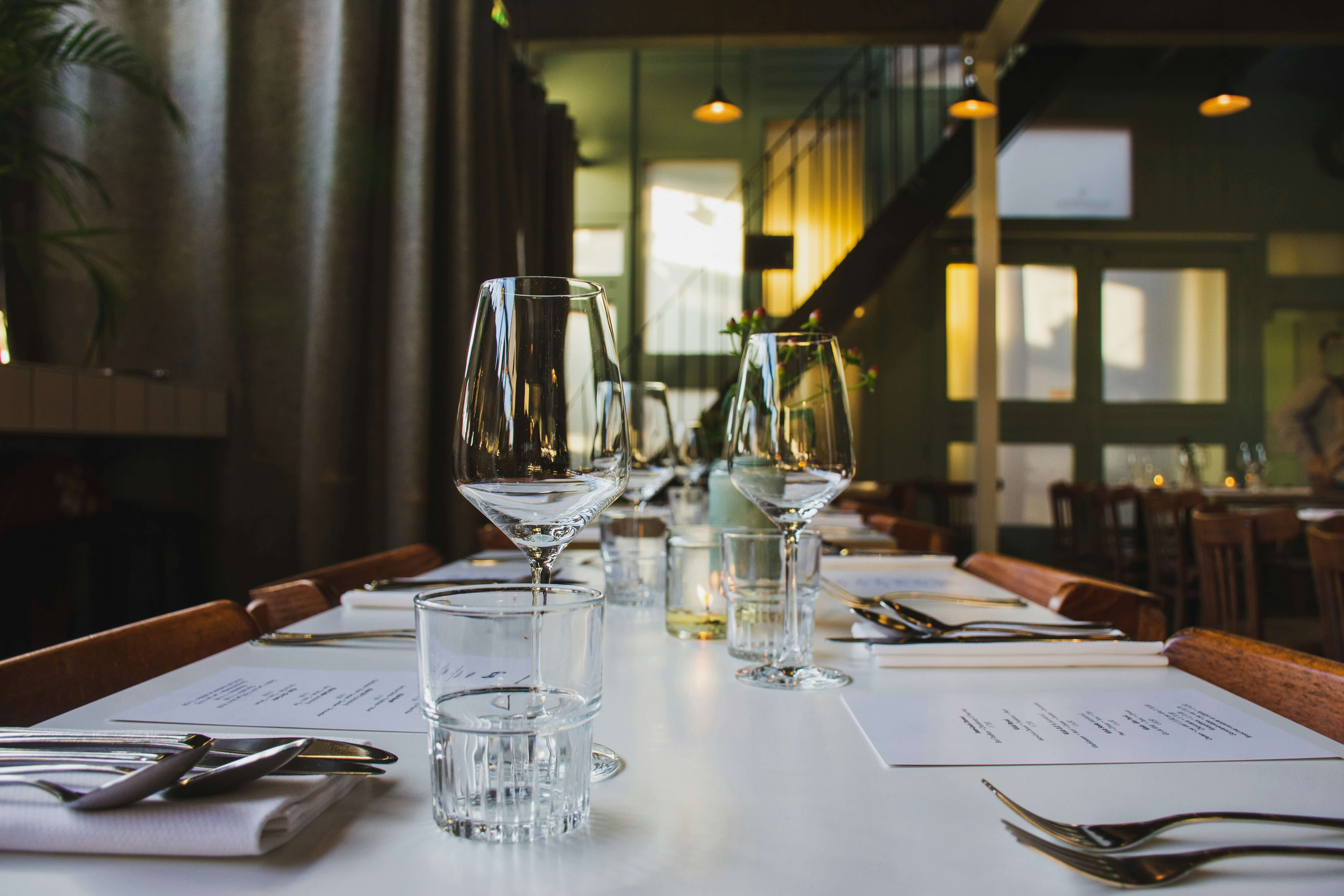 There is a table set for dinner and there is a slightly blurred effect on the image. The table is white and there are whine glasses, cutlery and napkins on the table for four pepole. 